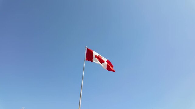 Slow motion footage of the Canadian flag blowing in the wind on a bright sunny day in Canada with clear blue sky in the summer time