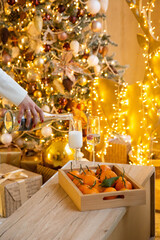 woman's hand pouring sparkling wine into the glass in front of a christmas tree