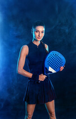 Sports portrait of active female player in motion holding padel racket under blue pink light in dark background
