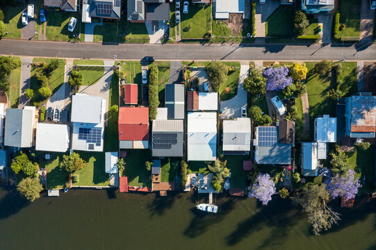 Top down aerial view of blooming jacaranda trees, gardens, and houses with private jetties and slipways along the water at Dora Creek in the Lake Macquarie region of NSW, Australia.