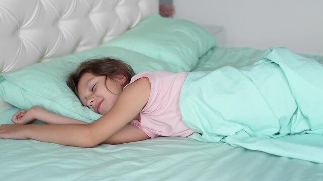 A little girl sleeps on a large bed in a bedroom with a modern renovation. The concept of waking up in the morning and starting a new day. 4k footage