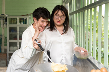LGBTQ friends, one with long hair and one with short, prepare a Thai-style omelette together in a cozy open kitchen. The scene captures their joyful moment of cooking for breakfast.