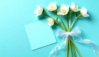 White spring flowers tied with ribbon and blank blue card on turquoise background with copy-space