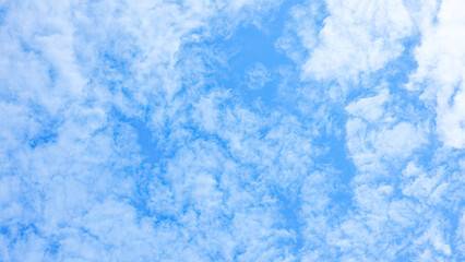 Bright blue sky background flled with scattered, fluffy white altocumulus clouds on a clear and sunny day, suitable for wide views.