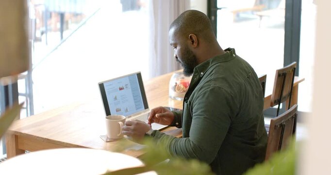 When reviewing laptop charts, man is pausing and sipping coffee from mug in cafe for focus