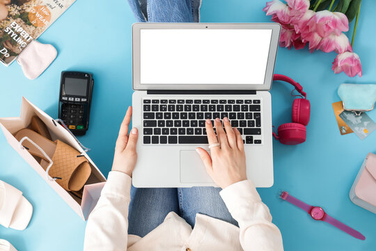 Woman with laptop and tulips shopping online on blue background, top view