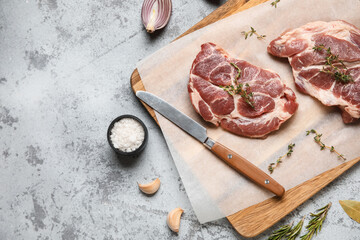 Wooden board with fresh raw steaks and different spices on grey background