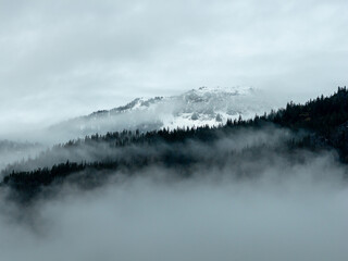 Misty Snowy Mountain Range Shrouded in Fog Over Conifer Forests in BC, Canada