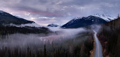 Naklejka premium Misty Valley Road Through Snowy Mountain Range in BC, Canada at Sunset