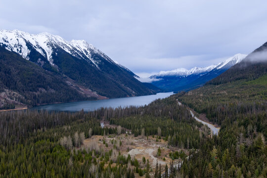 Snow-Capped Mountain Range Over a Serene Lake in BC, Canada, Surrounded by Dense Forest - Powered by Adobe