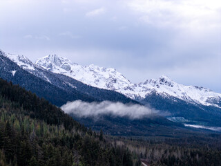 Snowy Mountain Range Over Forested Valleys in BC, Canada During Winter Scene With Clouds Majesty