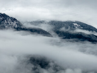 Snowy Mountain Ridge Shrouded in Mist Over Cloudy Valley in British Columbia
