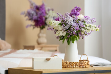 Vase with lilac flowers and box on bench in bedroom