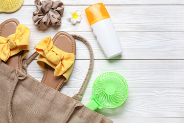 Bag with female summer accessories and mini fan on white wooden background