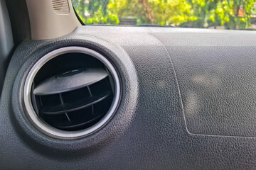 Close up of a car interior air conditioning vent with textured dashboard and blurred outdoor greenery background