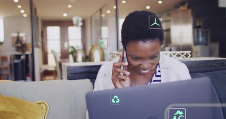 Woman in living room answering work call, leaning to laptop and reading floating green eco icons - Powered by Adobe