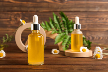 Bottle of cosmetic product and chamomile flowers on wooden background, closeup