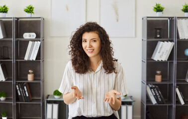 Portrait of a young woman standing in office having online webinar or video call with colleague or...