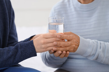 Caregiver giving senior woman glass of water in bedroom, closeup. Care concept