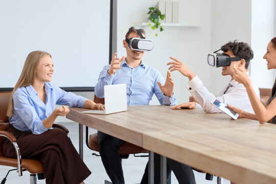 Young business colleagues using VR glasses at table in office