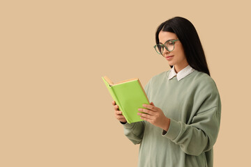 Fototapeta premium Beautiful woman in eyeglasses reading book on beige background