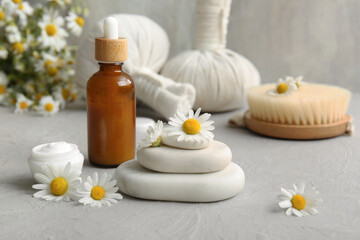 Composition with spa stones, chamomile flowers, bowl and bottle of cosmetic products on grey grunge background, closeup