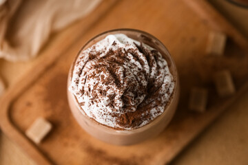 Glass of cocoa drink with whipped cream and powder on brown background