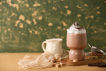 Glass of cocoa drink with whipped cream and sugar cubes on brown table against green grunge wall