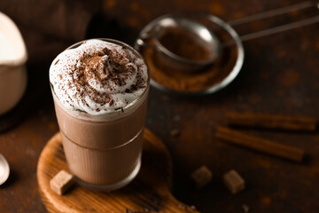 Glass of cocoa drink with whipped cream, cinnamon sticks and sugar cubes on red grunge background