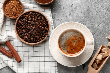 Cup of coffee with beans, cinnamon sticks and sugar cubes on grey grunge background