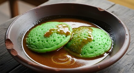 Delicious traditional green pancakes drizzled with rich palm sugar syrup, presented beautifully in a rustic brown bowl, an authentic sweet treat from Southeast Asian culinary traditions