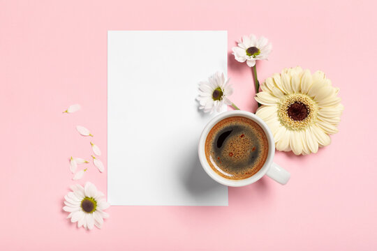 Cup of coffee with gerbera flowers and blank card on pink background