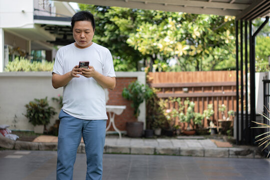 A man stands outdoors using his smartphone in a calm home environment. Natural light and greenery highlight a simple modern lifestyle.