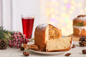 Plate with cut Christmas Panettone, star anise, cinnamon sticks, cones and decor on tile table against blurred lights