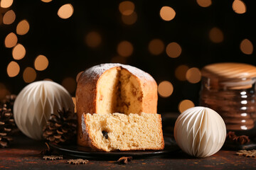 Cut Christmas Panettone with star anise, cones and paper balls on red grunge table against blurred lights