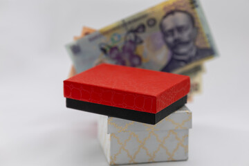 red and black jewelry box sits atop a decorative white box, with romanian lei banknotes visible in the background, suggesting concepts of gift-giving and luxury