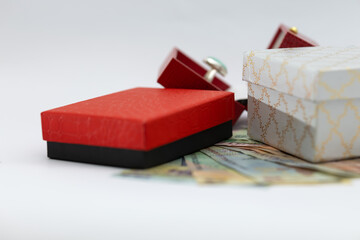 small red and white gift boxes with jewelry and scattered money on a white background, symbolizing expensive gifts, luxury, spending, and financial exchange