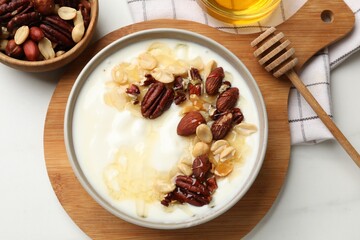 Delicious Greek yogurt with honey and nuts served on white table, flat lay