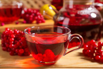 Glass cup of hot viburnum tea on wooden background, closeup