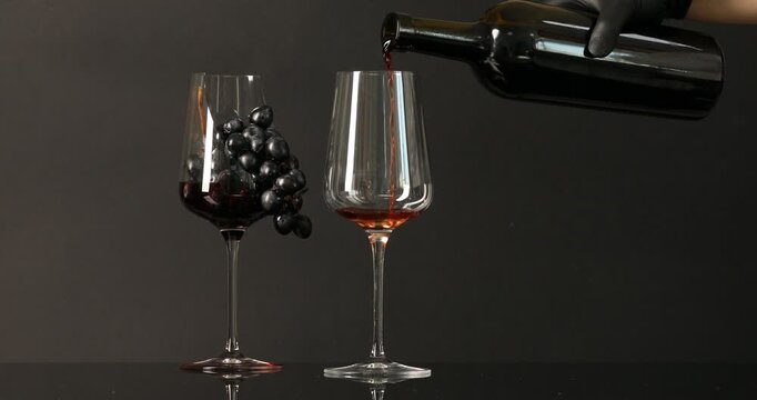 Woman pouring red wine into glass on black background, closeup
