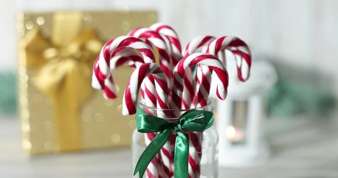 Merry Christmas and Happy New Year. Jar with tasty candy canes, gift box and lantern on white wooden table, closeup. Camera moving up