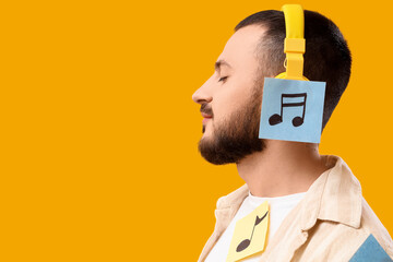 Young man in headphones with paper music notes on yellow background, closeup