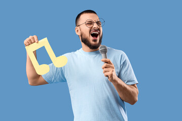 Young man with paper music note and microphone singing on blue background
