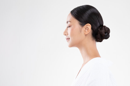 Asian serene woman profile portrait closed eyes bun hairstyle white robe meditative expression calm skin studio session wellness minimal background