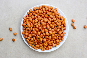 Raw, shelled peanuts piled on a white plate, ready for roasting.