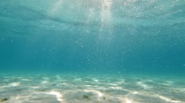 A wide angle view of the deep blue ocean captures sunlight reflecting through underwater waves and ripples against a summer horizon where the sea meets a bright sky of white clouds