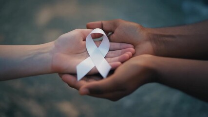 Diverse hands passing a white ribbon, a symbol of hope and awareness for lung cancer, safe motherhood, or violence against women in a supportive gesture