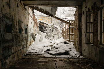 Abandoned industrial hall in winter with collapsed roof and snow piles inside