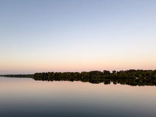 Calm river with tree line and soft pastel sky background
