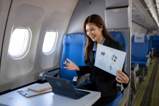 Asian businesswoman doing video call on airplane presenting charts